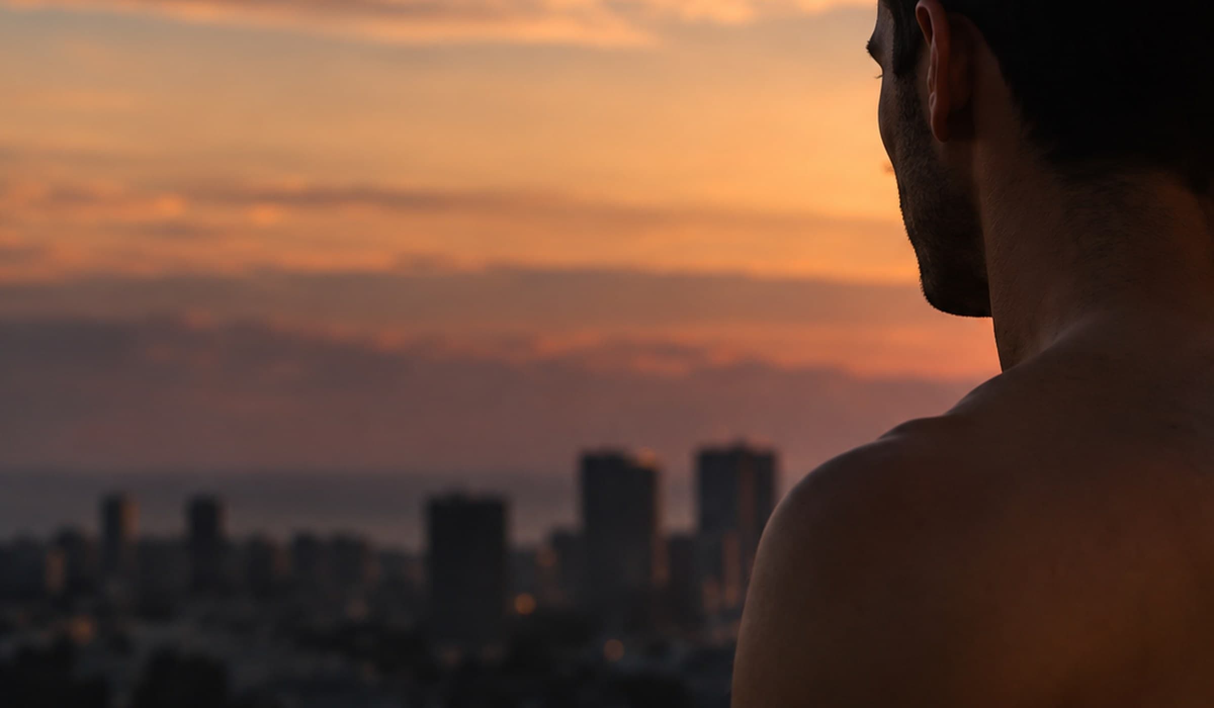 A man alone at a window at dusk, seen from behind