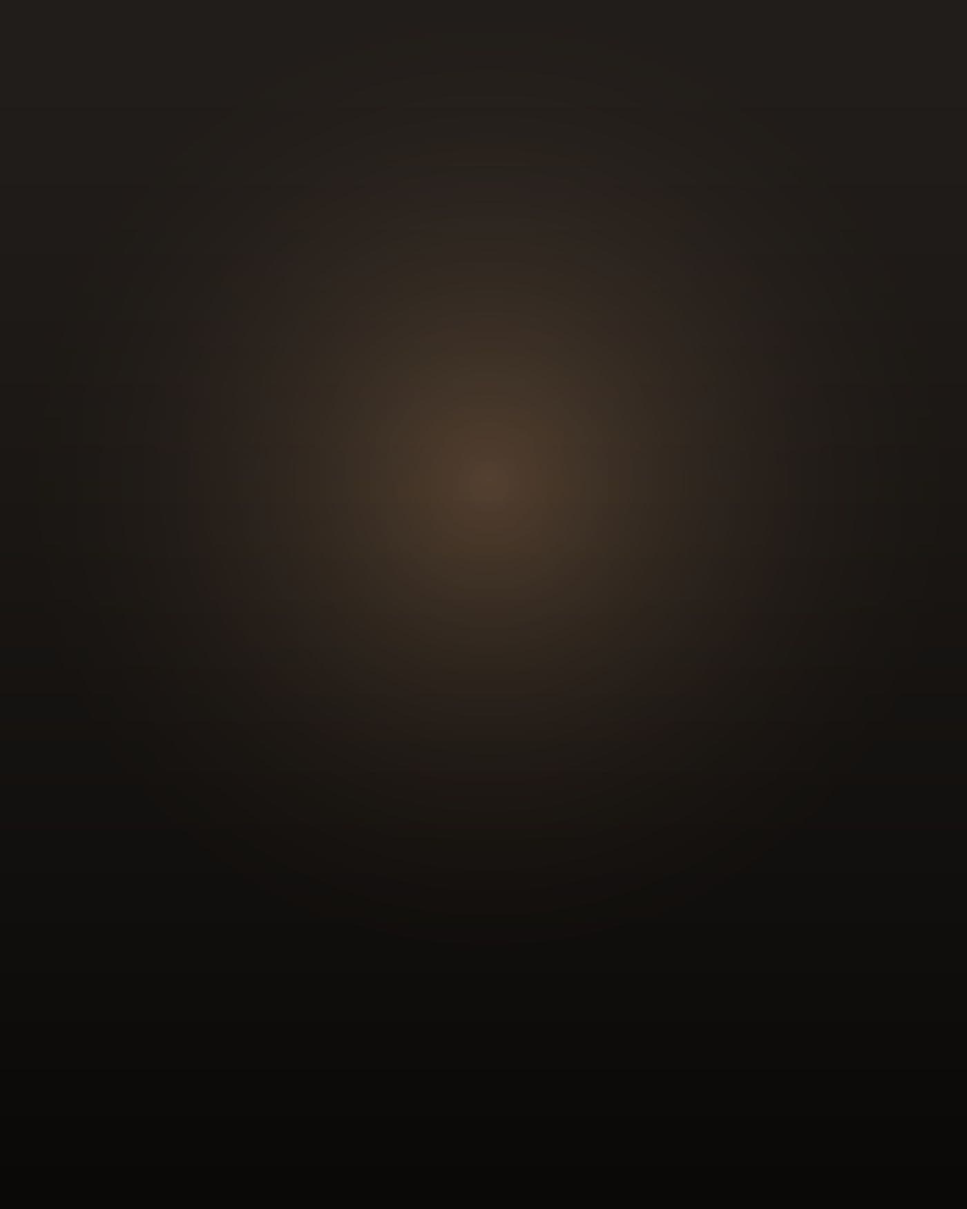 A Black man of about forty-four, Nigerian American, tall and heavy through the chest and shoulders with a thick neck, shaved head and a short greying beard, standing on a hospital stairwell landing at night in navy scrubs, one hand on the rail, turned away from the camera, lit low and warm from an open doorway with the rest of the frame in deep shadow.