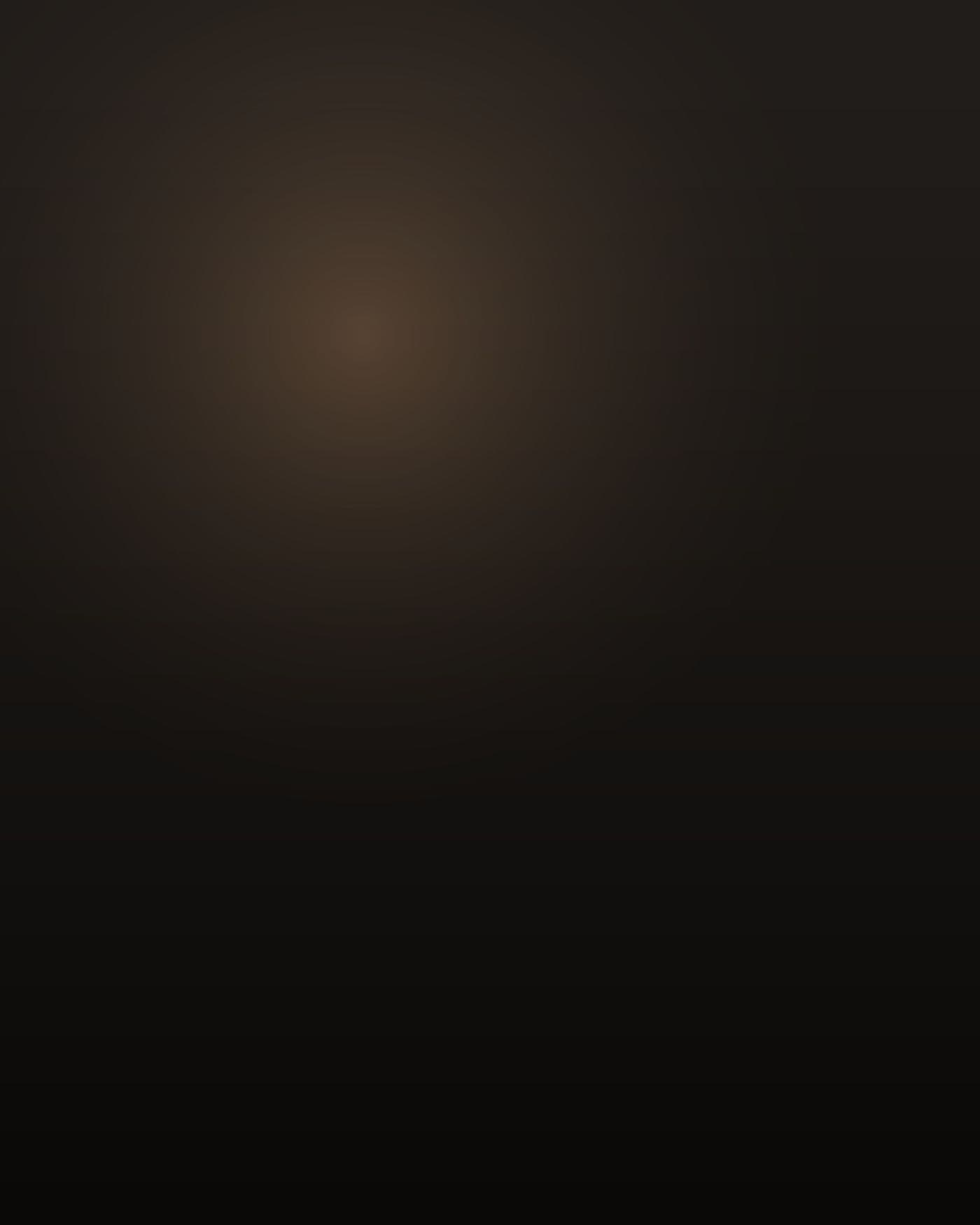A South Asian man of about twenty-six, Pakistani, thick and heavyset through the chest and middle, short, head shaved bald, a thin dark beard, sitting on the edge of a single bed in a narrow back bedroom, turned away toward a bare drywall wall so his face is not visible; low warm light from a streetlamp through the blinds, most of the room in deep shadow, a phone charger cable on the floor.
