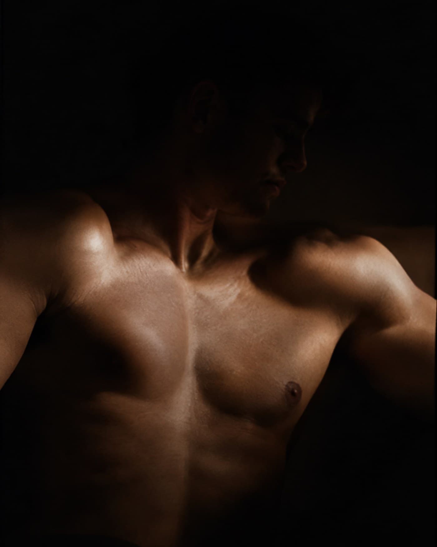 A man in his early fifties standing alone at a workbench in an open garage at dusk, one hand resting on a pulled-out tool drawer, lit by a single bare bulb, a dark desert street behind him.